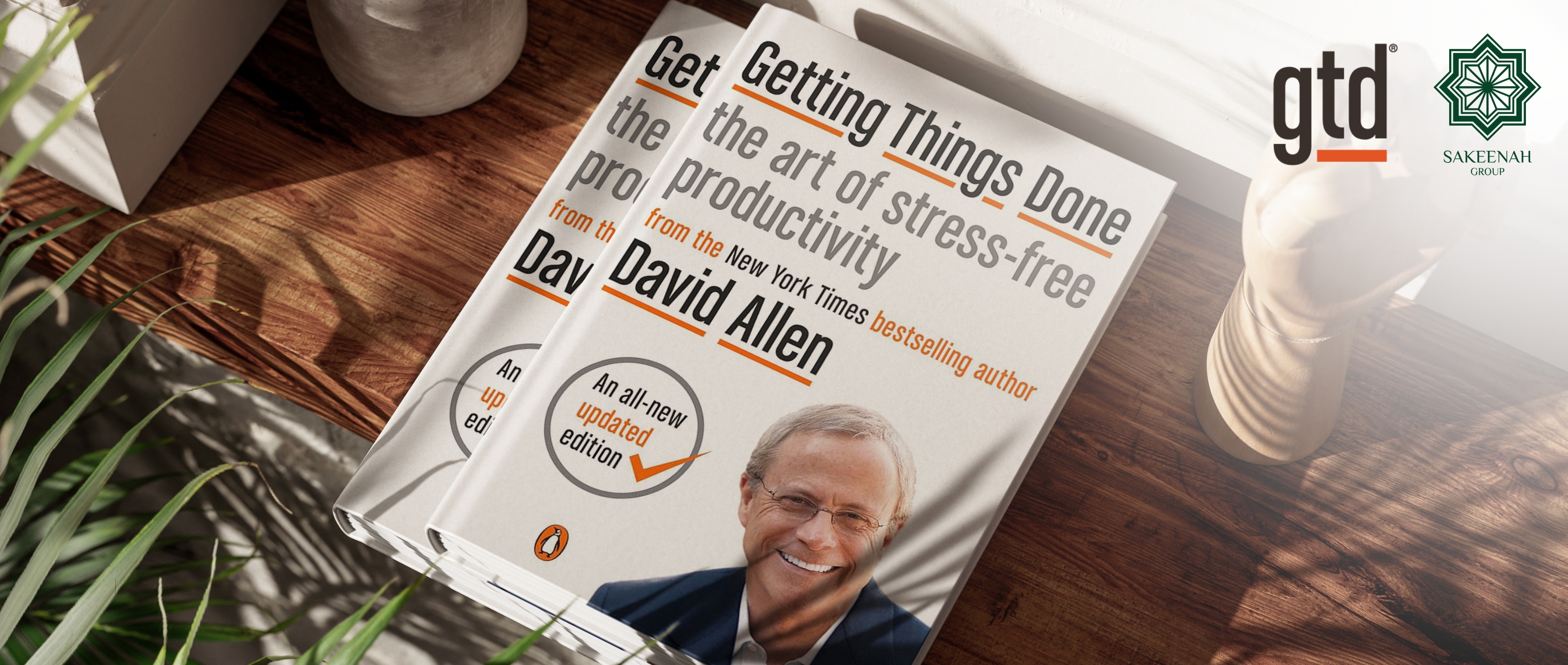 Two copies of David Allen’s book, 'Getting Things Done: The Art of Stress-Free Productivity', resting on a sunlit wooden surface. The image features the book's updated edition cover, the GTD logo, and the Sakeenah Group logo.